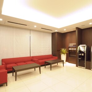 A modern waiting area with a red sofa set, a coffee table, a potted plant, and a self-service kiosk. - Ab Hotel Omihachiman (Omihachiman)