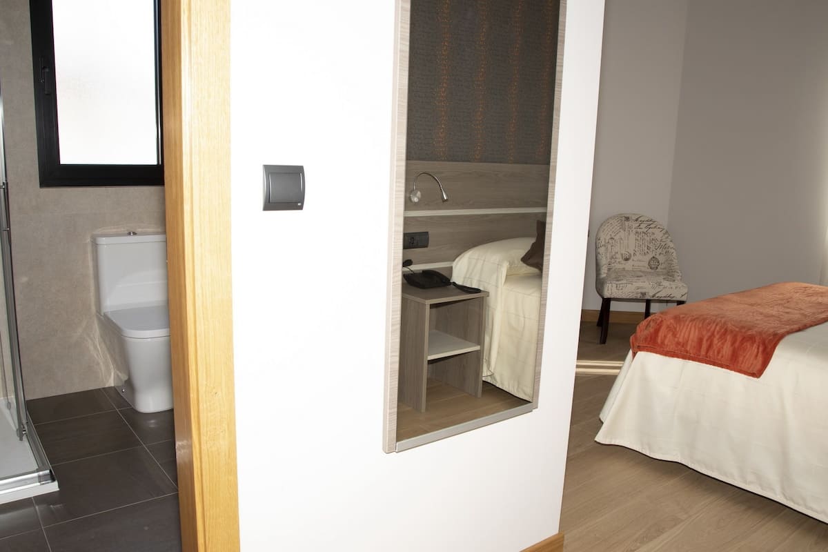 A hotel room with a bed, a desk with a chair, a shower area, and a toilet.