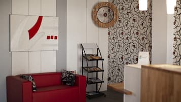 A modern room with a red sofa, a wall clock, a patterned wallpaper, and a magazine rack.