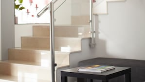 Un interior modern amb una escala, una barana de vidre, una taula petita amb un llibre i un mapa del món a la paret.