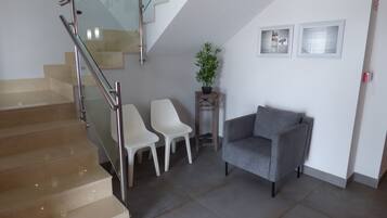 A staircase with glass railings, a grey armchair, two white chairs, and a small wooden table with a plant.
