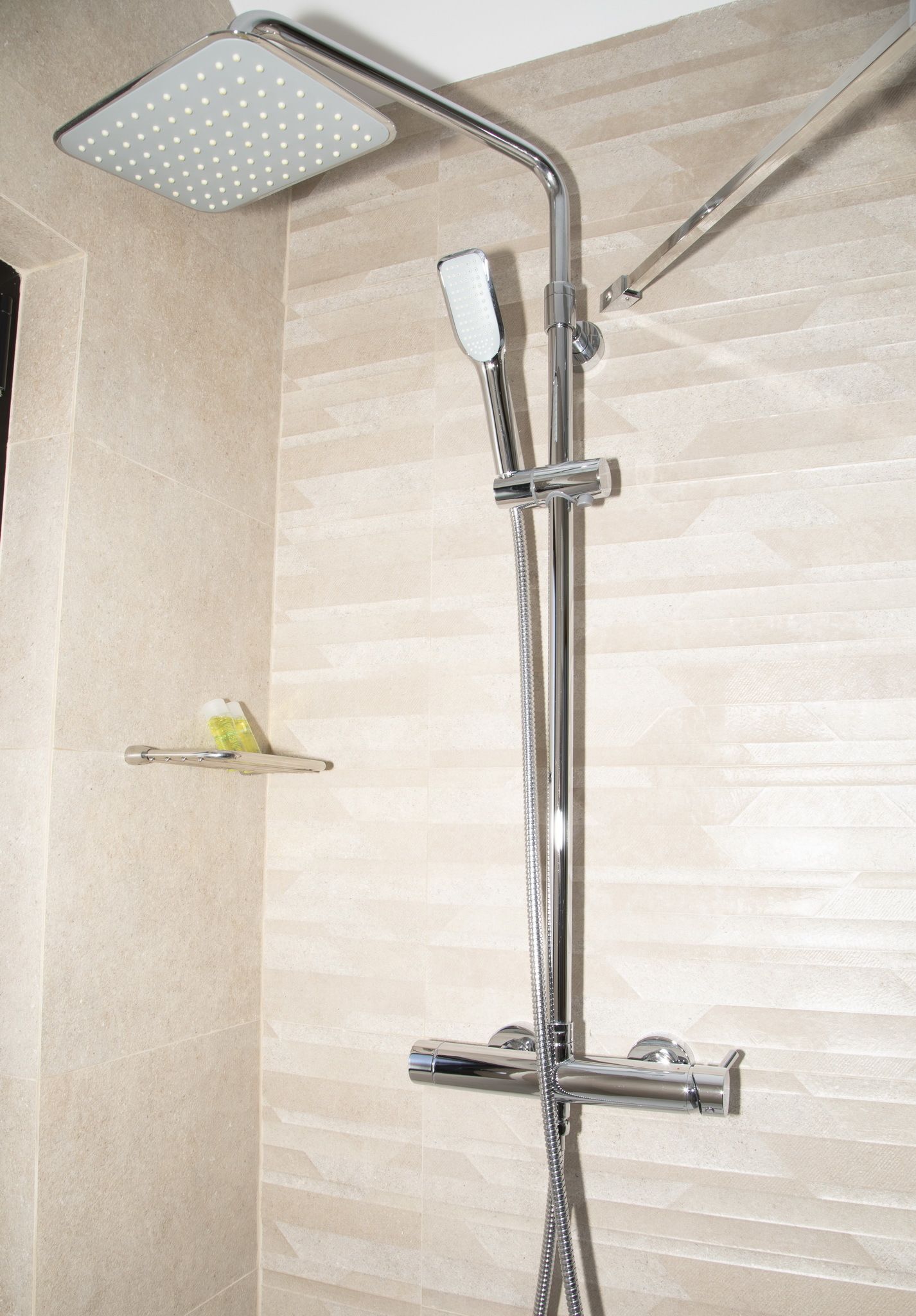 A modern shower with a square head, a handheld showerhead, and a handheld faucet.
