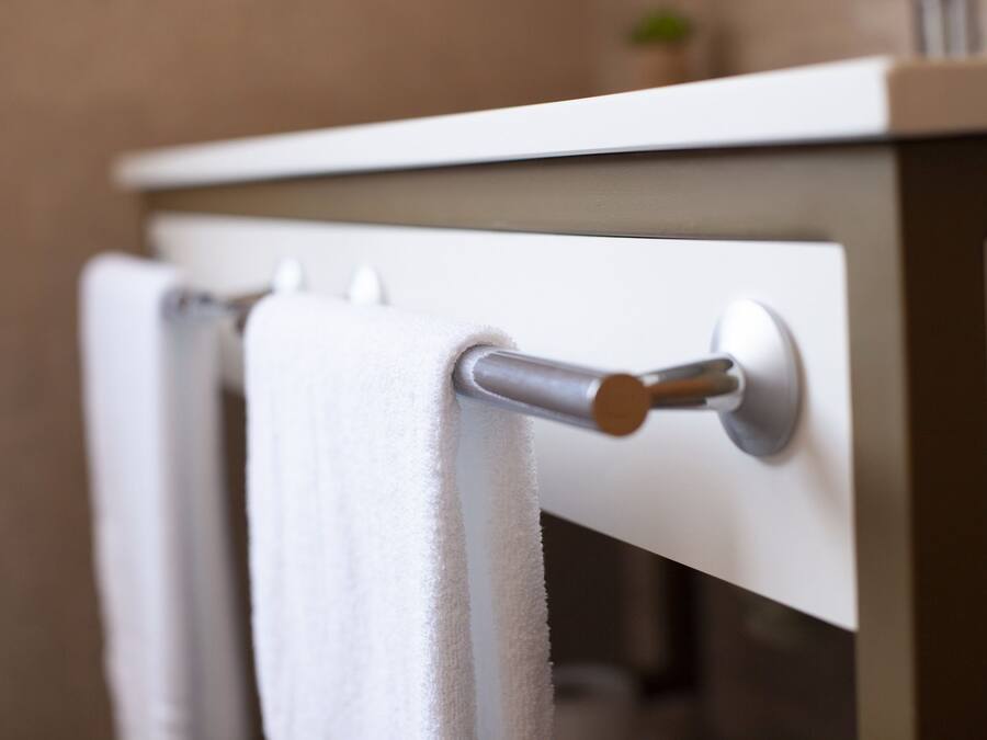 A white towel hanging on a metallic towel bar attached to a white wall.