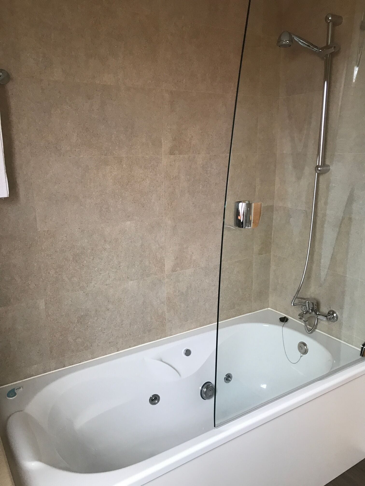 A modern bathroom with a freestanding bathtub, a glass shower enclosure, and beige tiled walls.