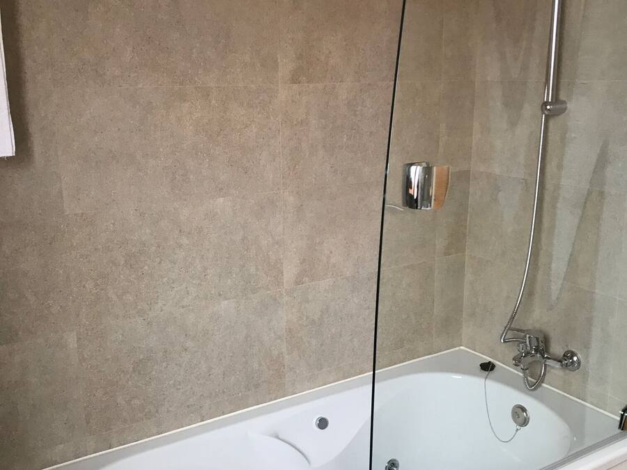 Un baño moderno con una bañera independiente, cabina de ducha de vidrio y paredes de azulejos color beige.