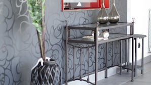 Un interior modern amb una paret decorativa, un mirall amb marc vermell, una taula de metall i una planta en test.