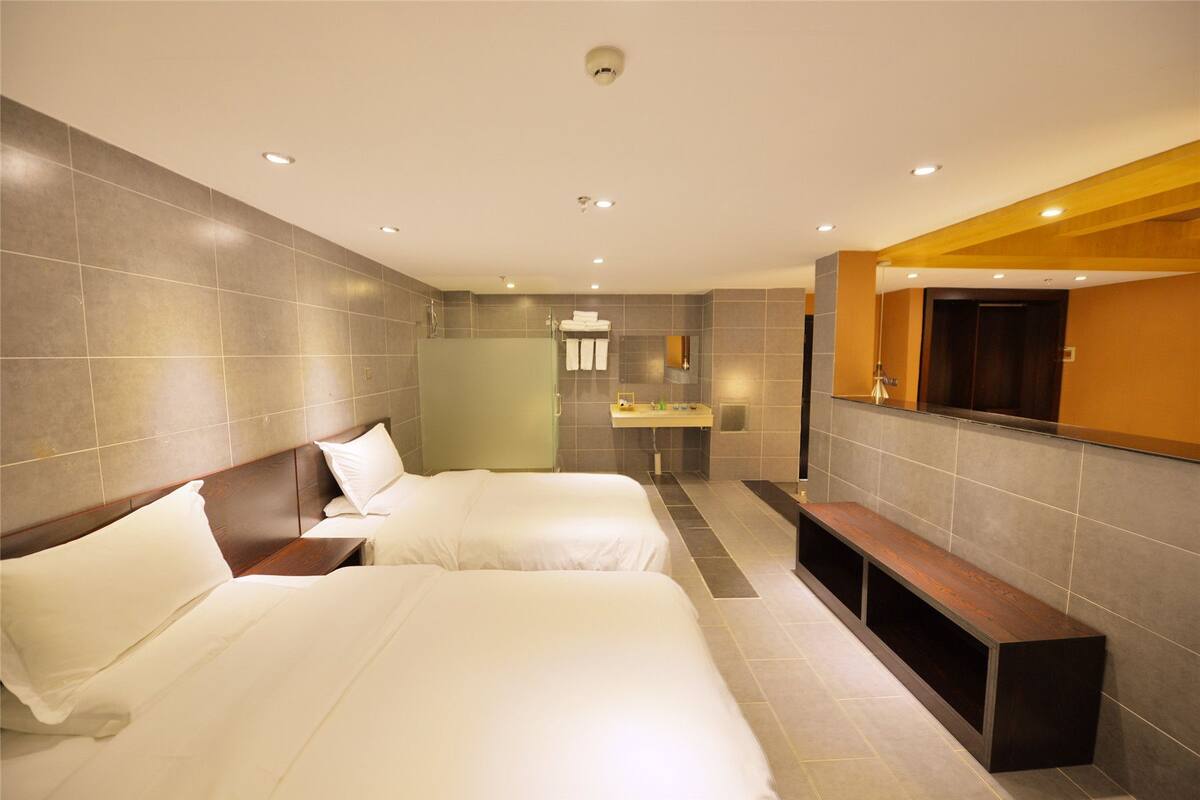 Habitación de hotel con dos camas, un banco, un lavabo y un espejo.