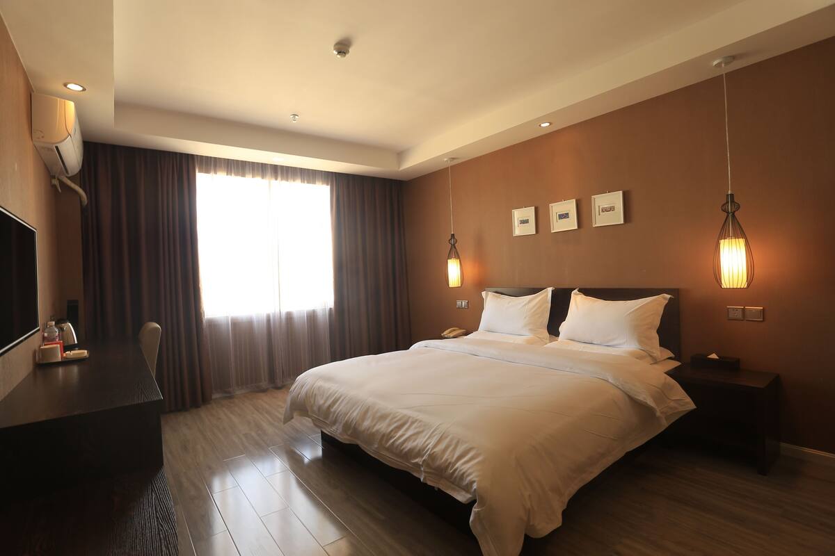 Habitación de hotel con una cama grande, un escritorio, una silla y un televisor. Hay dos mesitas de noche con lámparas y un televisor instalado en la pared.