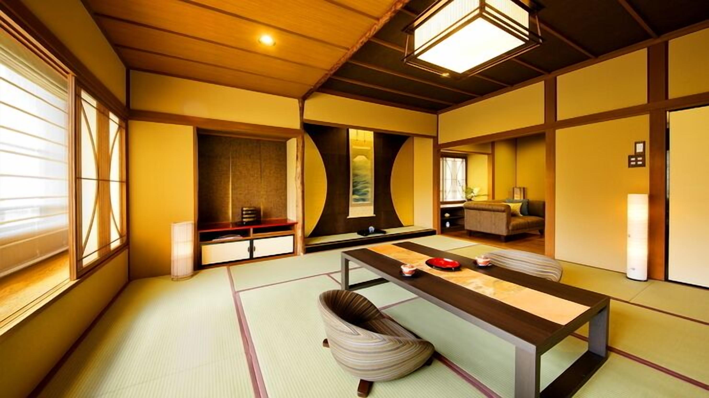 Una habitación tradicional japonesa con suelo de tatami, una mesa baja, zona de estar con cojines y puertas correderas.