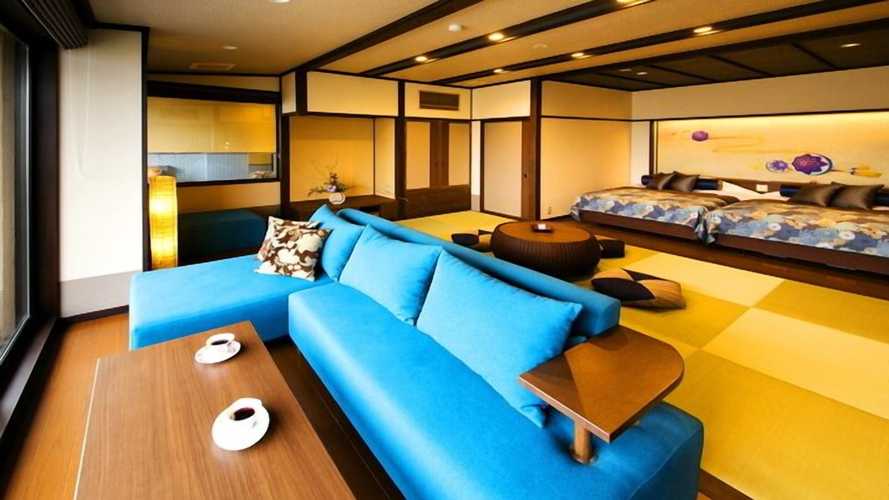 A modern interior with a blue sofa, a wooden coffee table, and a bed with patterned bedding.