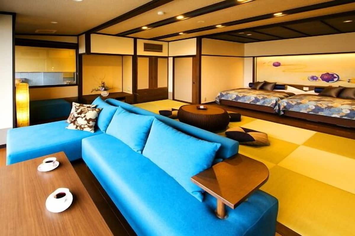 A modern interior with a blue sofa, a wooden coffee table, and a bed with patterned bedding.