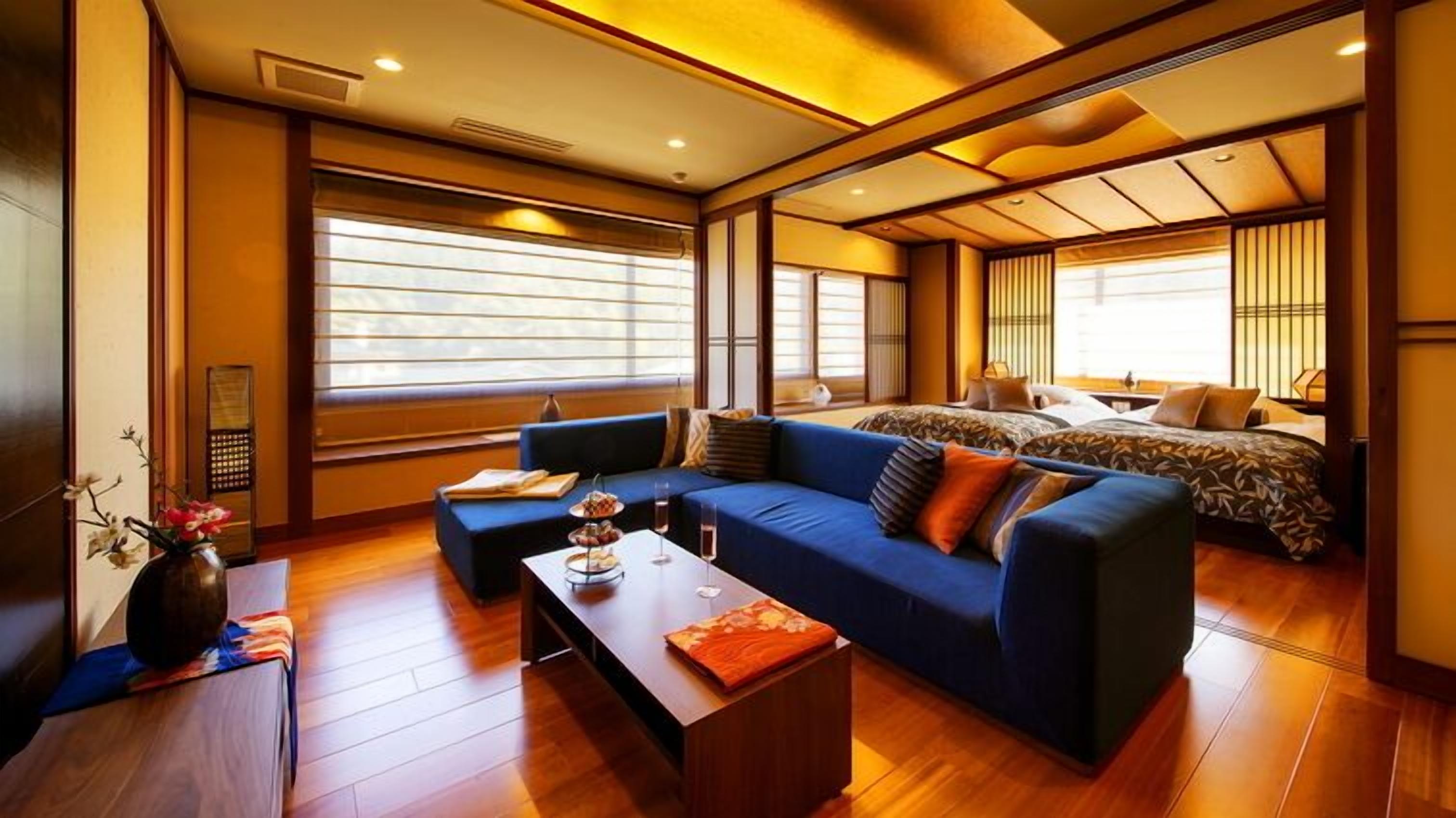 A modern hotel room with a sofa, a bed, a coffee table, and large windows.