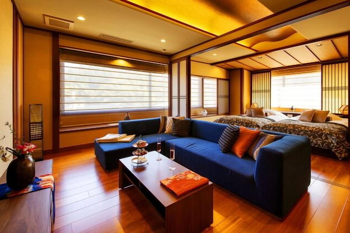 A modern hotel room with a sofa, a bed, a coffee table, and large windows.