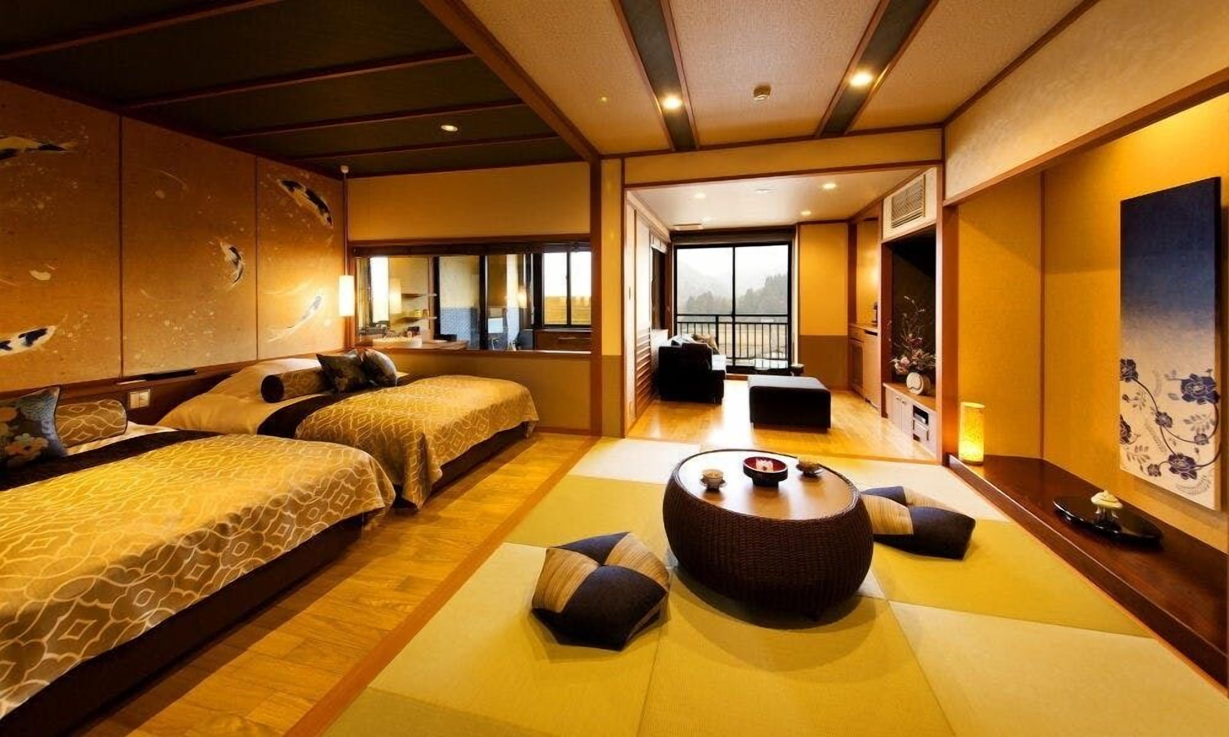 A traditional Japanese-style hotel room with tatami flooring, two beds, a tatami mat seating area, and a large window with a view.