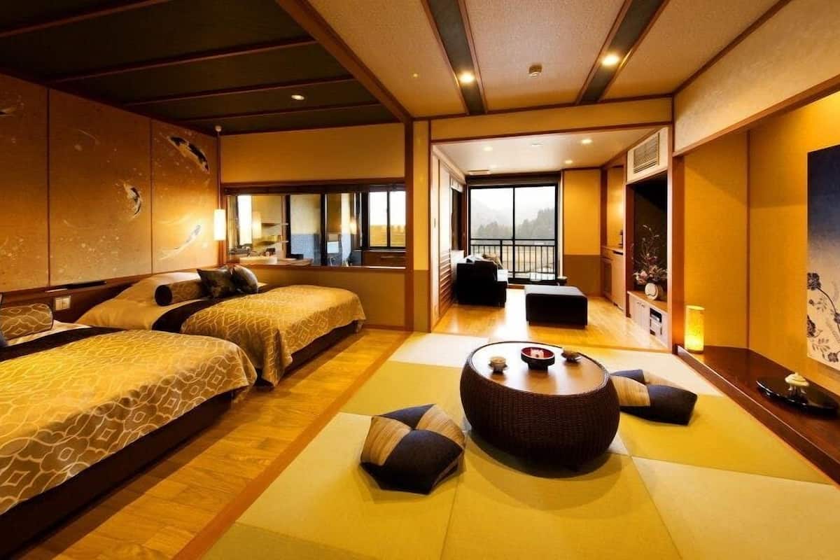 A traditional Japanese-style hotel room with tatami flooring, two beds, a tatami mat seating area, and a large window with a view.