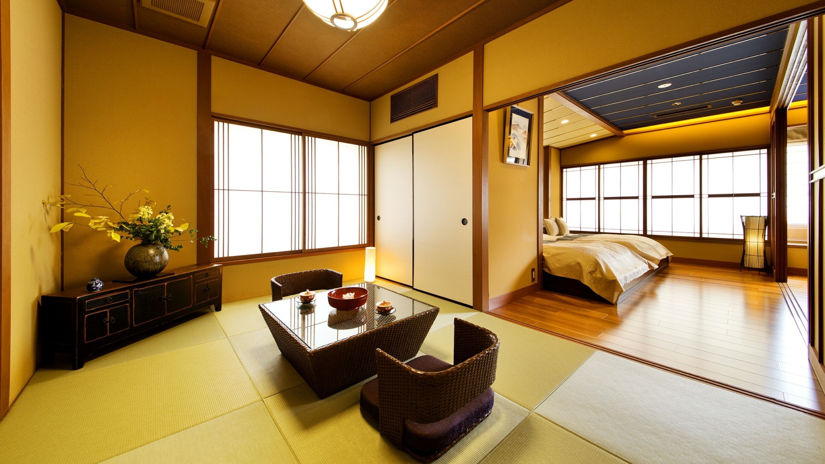 Ein traditioneller japanischer Raum mit Tatami-Bodenbelag, einem niedrigen Tisch mit Vase und Schüssel sowie einem Bett mit Futon.