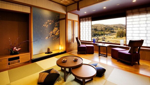 A traditional Japanese-style room with tatami flooring, a low table with cushions, a large window with a view of a mountainous landscape, and a sliding door with a cherry blossom painting. - Kanazawa Yuwaku Onsen Hyakurakuso (Kanazawa)