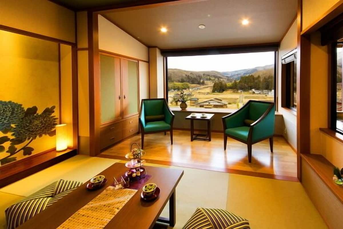 A room with a dining table, two green chairs, a view of a mountainous landscape through large windows, and traditional decor.