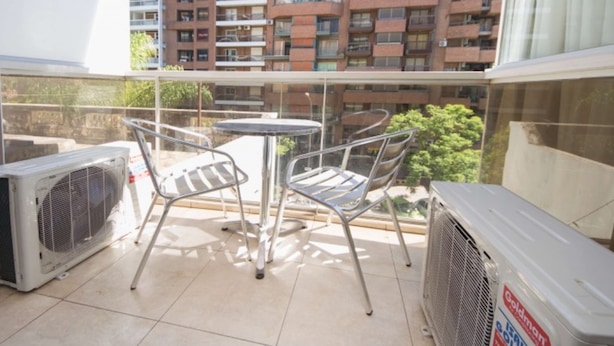 A balcony with a table and chairs, air conditioning units, and a view of a high-rise building with multiple balconies. - Obispo Oro Flat ZX3 (Córdoba)