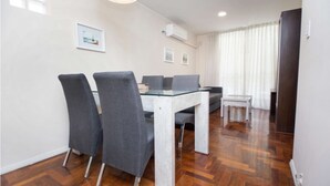 A modern dining area with a glass table and grey upholstered chairs, wooden parquet flooring, and a large window with curtains. - Obispo Oro Flat ZX3 (Córdoba)