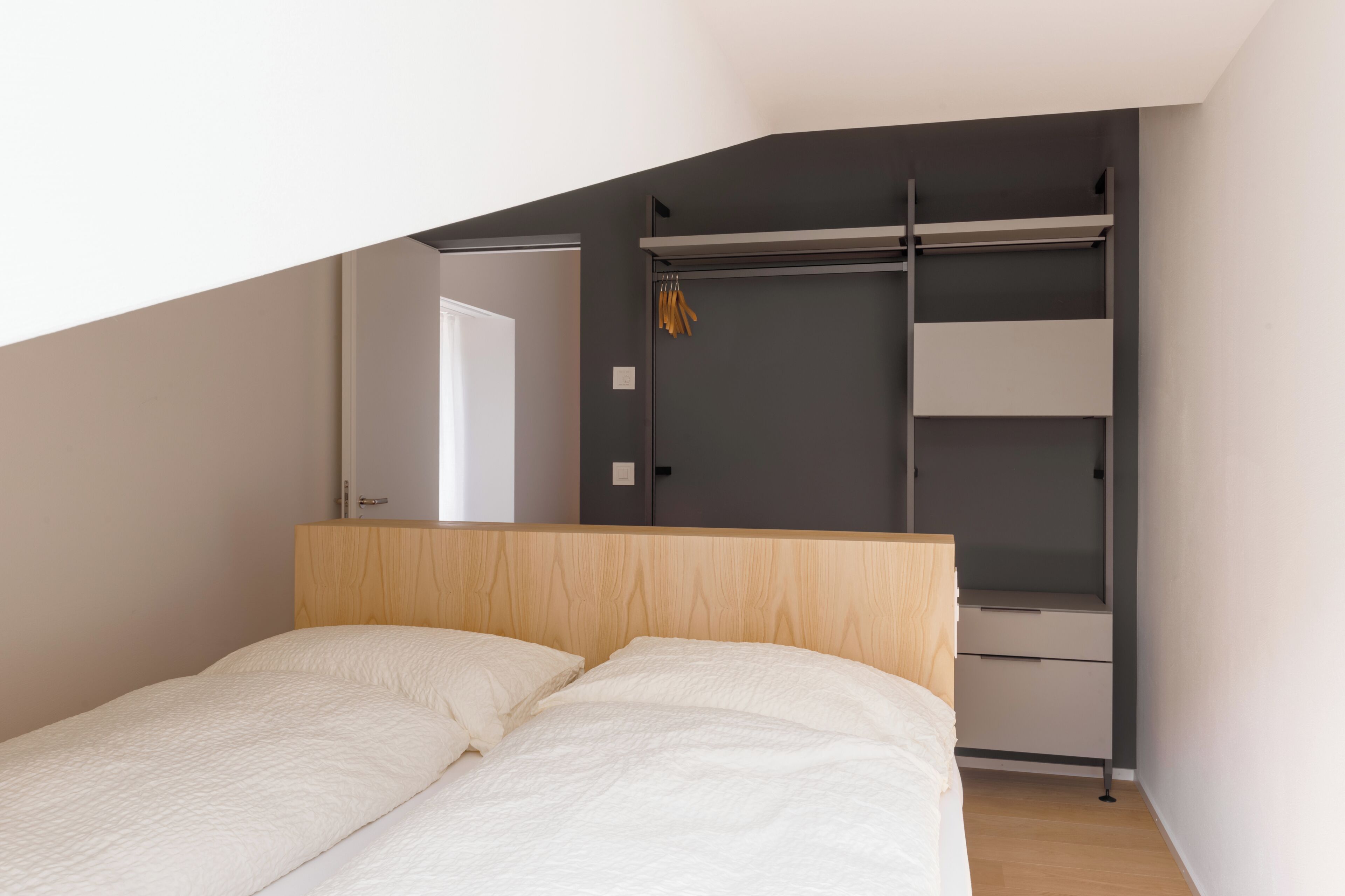 A bedroom with a bed, a wooden headboard, a grey wardrobe, and a white door.