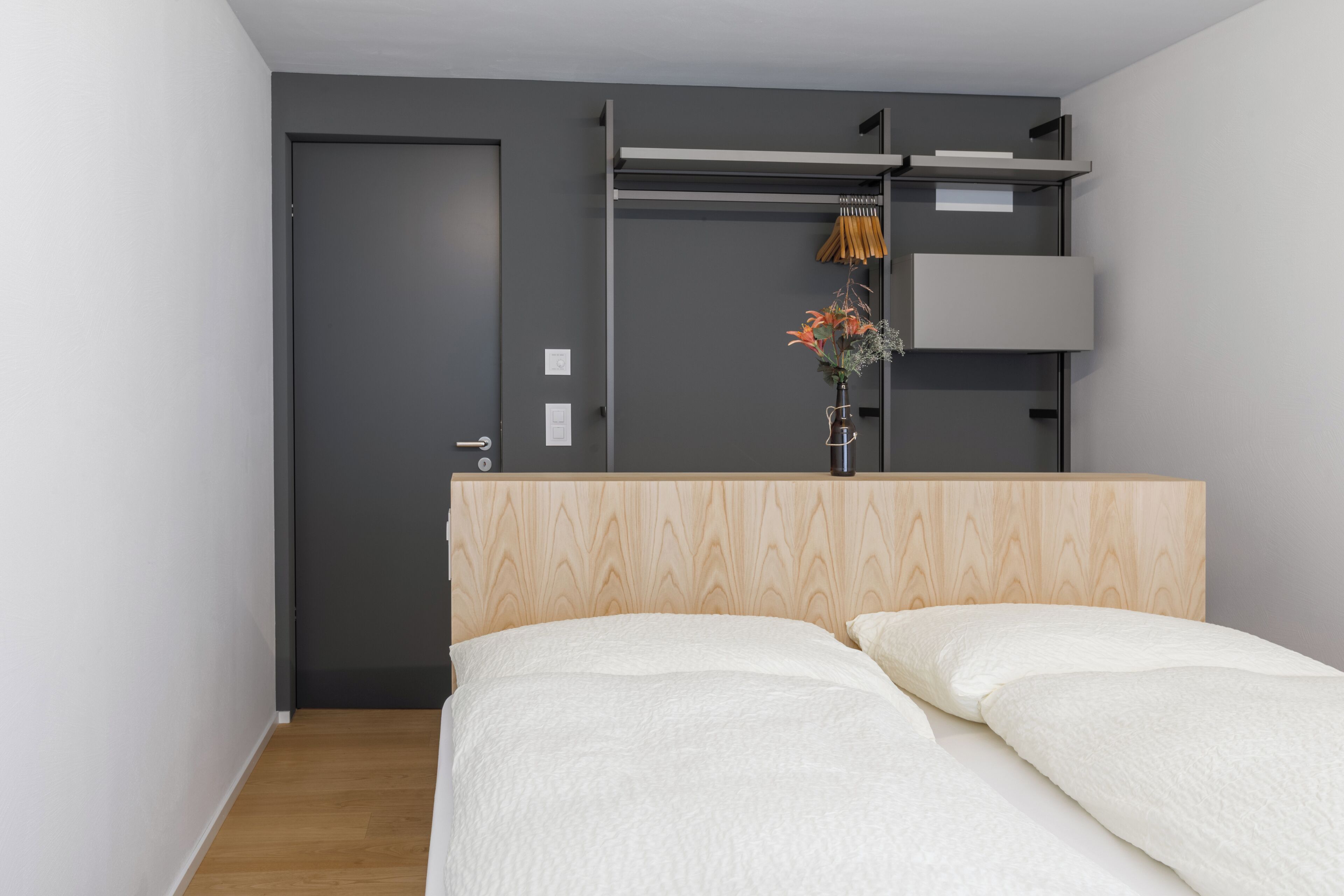 Une chambre à coucher comprenant un lit, une armoire et une étagère fixée au mur, sur laquelle est posé un vase de fleurs.