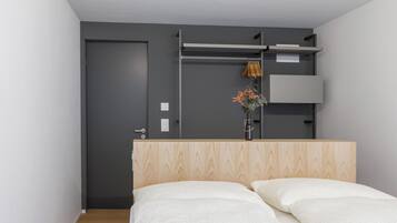 Une chambre à coucher comprenant un lit, une armoire et une étagère fixée au mur, sur laquelle est posé un vase de fleurs.