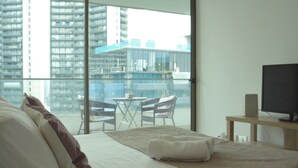 A hotel room with a large bed, a TV, a small table, and a balcony with a view of high-rise buildings. - Loica Suites (Santiago)