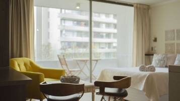 Enjoy a room with a large window offering a view of a nearby building, featuring a comfortable bed, two chairs, and a small table.