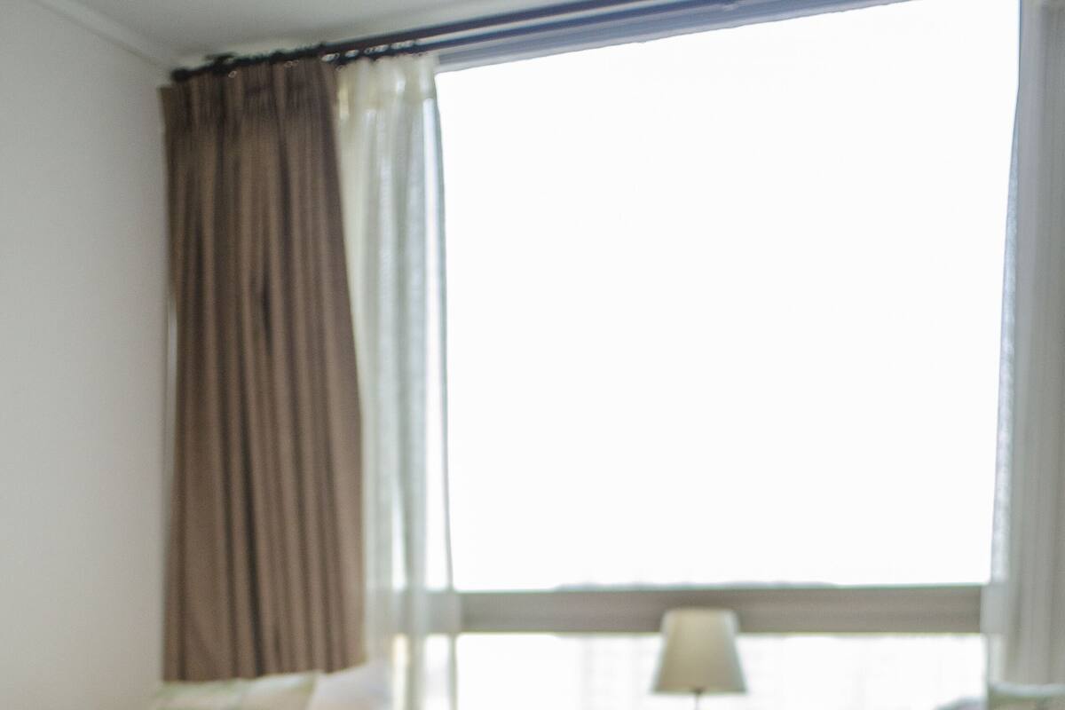Ein Schlafzimmer mit zwei Betten, einem Nachttisch, einer Lampe und einem Fenster mit Vorhängen.
