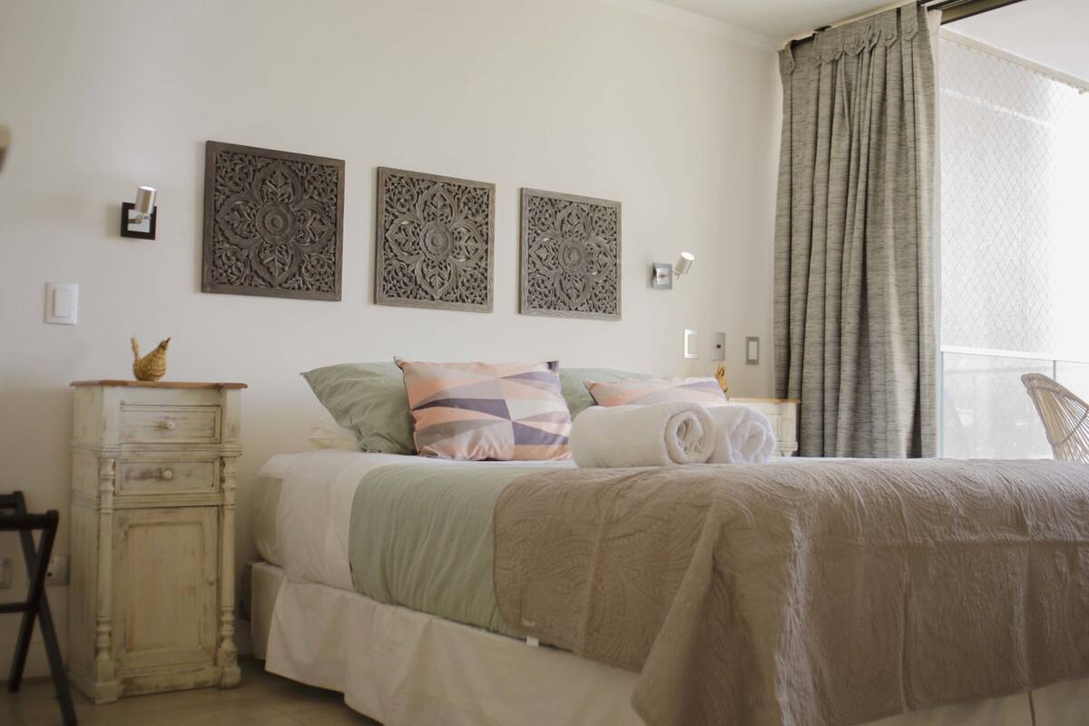 Ein Schlafzimmer mit einem Bett, einer Kommode, Wanddekoration und einem Fenster mit Vorhängen.