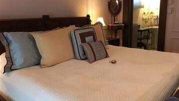 Un lit bien fait, recouvert d’une courtepointe blanche, avec une tête de lit en bois et plusieurs coussins aux motifs et couleurs variés.