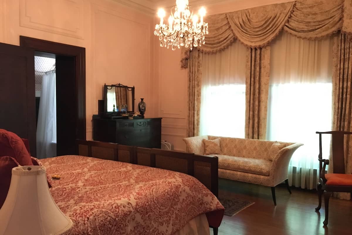 A bedroom with a large bed, a dresser, a chair, and a chandelier.