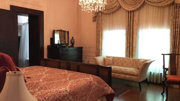 A bedroom with a large bed, a dresser, a chair, and a chandelier.