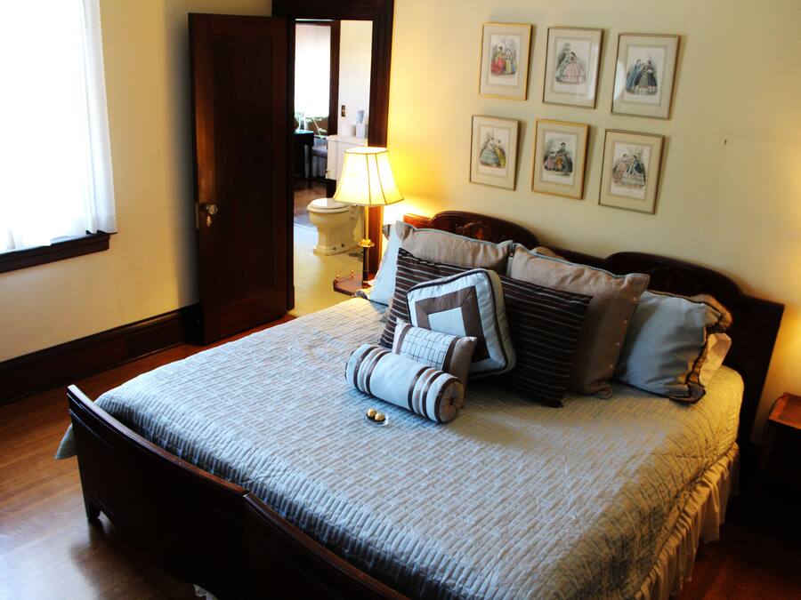 A neatly made bed with a striped bedspread and several pillows, a bedside table with a lamp, and a wall with framed pictures.
