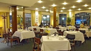 A dining area with multiple tables set for service, large windows, and a chandelier. - Hotel Cervantes (Mendoza)