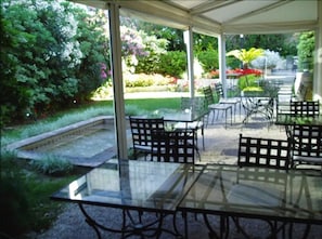 An outdoor patio with glass tables and chairs, surrounded by lush greenery and a garden. - Hotel Cervantes (Mendoza)