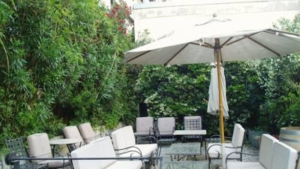 An outdoor patio with white cushioned seating, a table, and a large umbrella. - Hotel Cervantes (Mendoza)