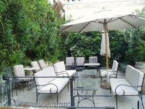 An outdoor patio with white cushioned seating, a table, and a large umbrella. - Hotel Cervantes (Mendoza)