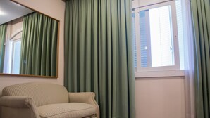 A room with a striped armchair, a window with blinds, and green curtains. - Hotel Cervantes (Mendoza)