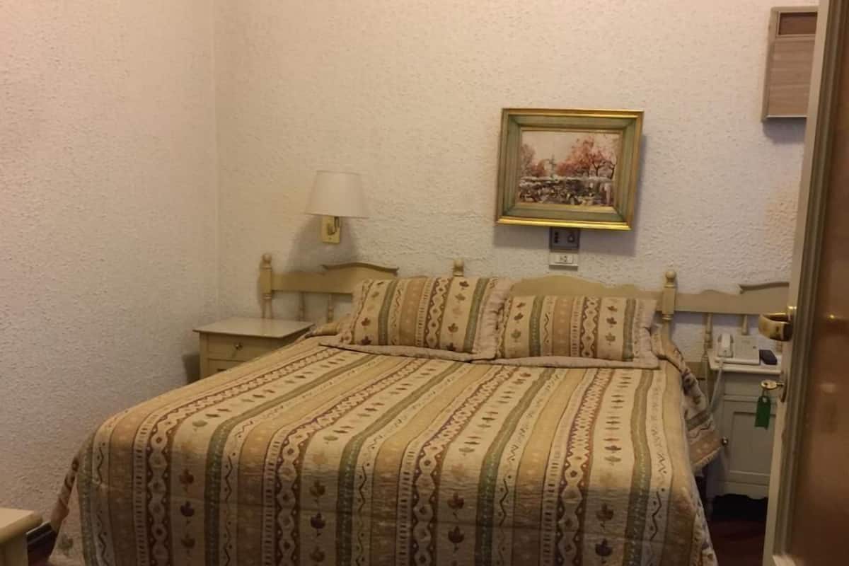 A bedroom with a wooden bed, a nightstand, a lamp, and a framed picture on the wall.