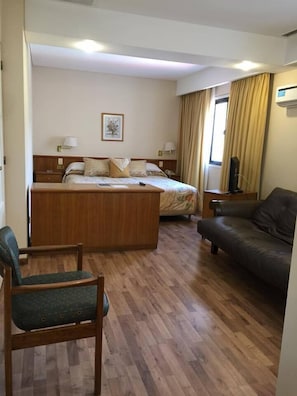 A hotel room with a bed, a desk, a chair, a sofa, and a window with curtains. - Hotel Cervantes (Mendoza)