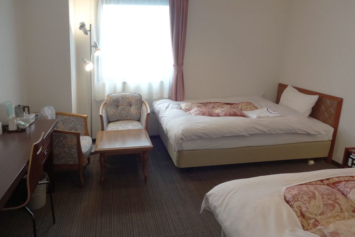 A hotel room with a bed, a chair, a desk, and a window with curtains.