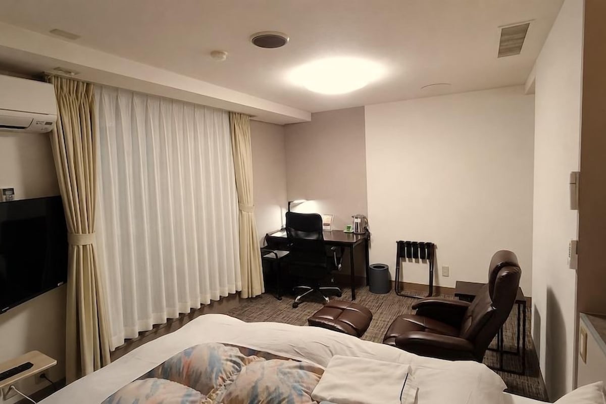 A hotel room with a bed, a desk, a chair, a TV, and curtains.