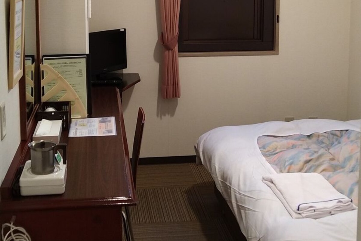 A hotel room with a desk, a bed, an air conditioning unit, a television, and a window with curtains.