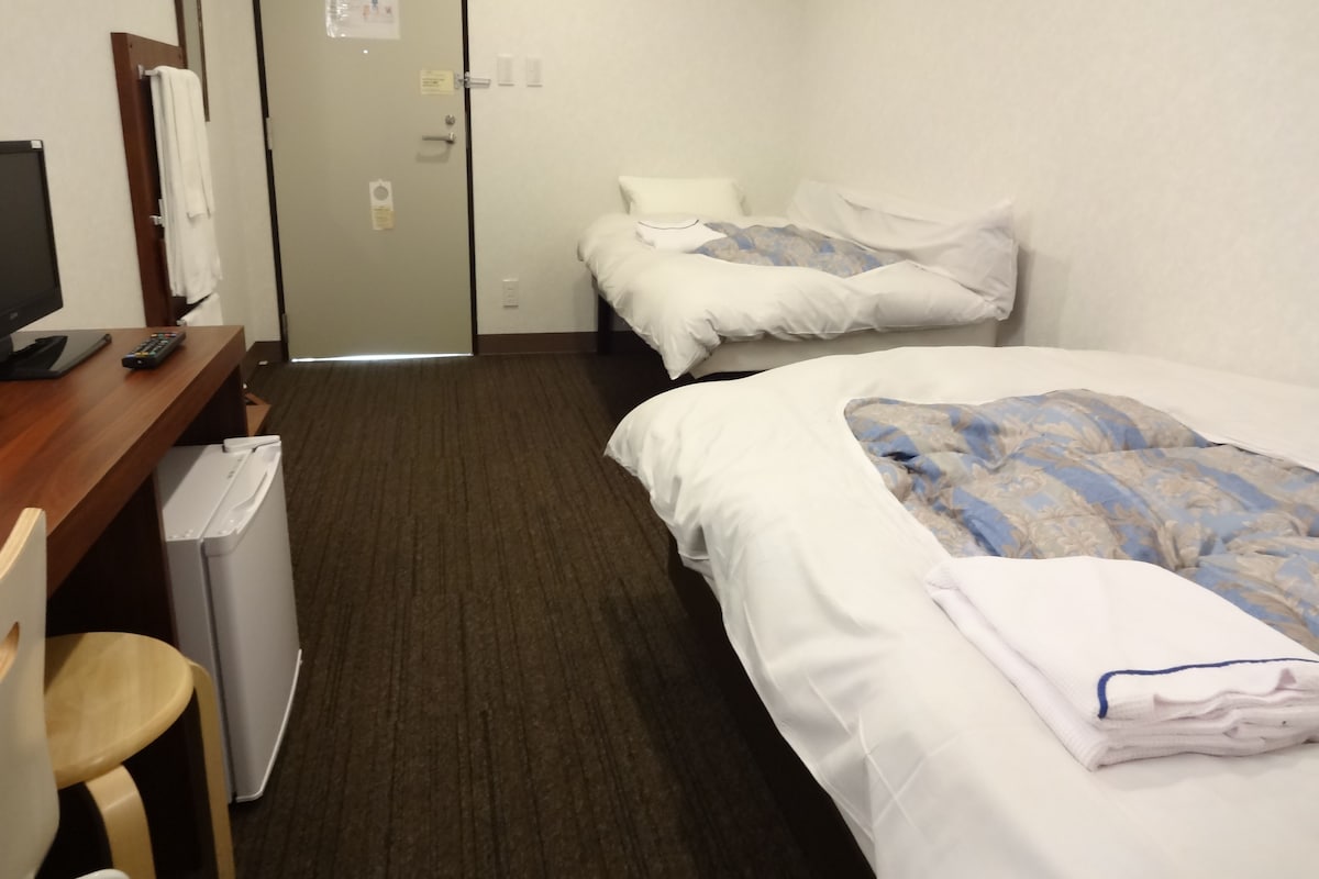 A hotel room with two beds, a desk with a computer, a chair, and a small table.