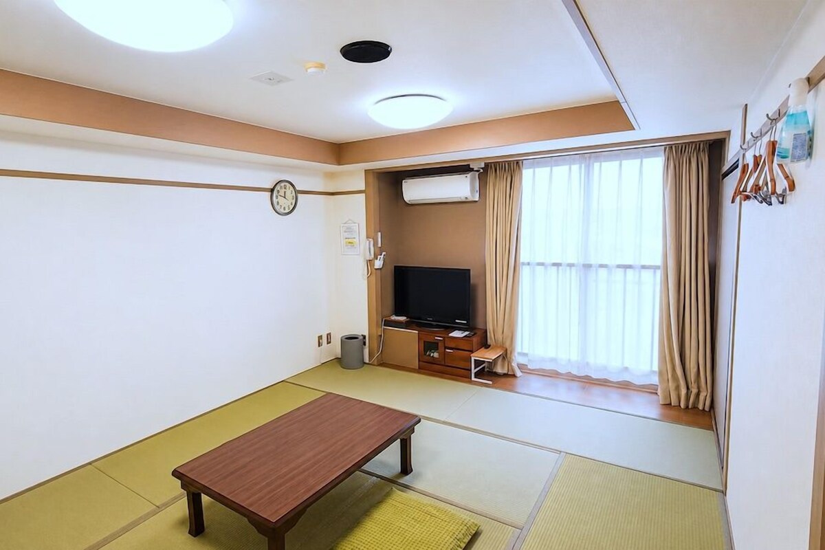 A room with tatami flooring, a television, a small table, and a window with curtains.