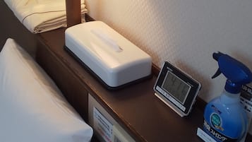 A hotel room with a bedside table, a lamp, a digital clock, a spray bottle, and a pillow.