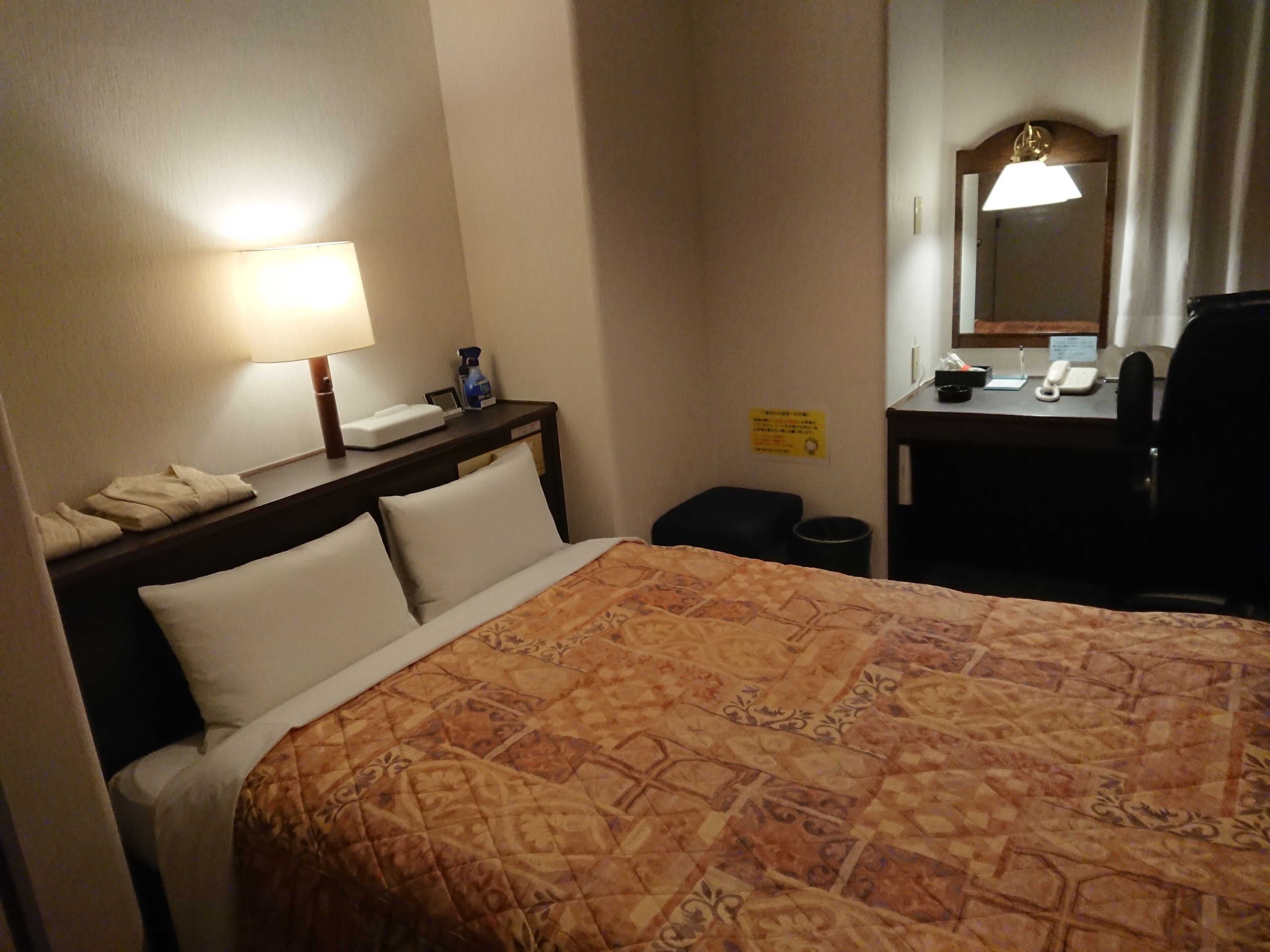 Una habitación de hotel con una cama, un escritorio con teléfono, un cesto de basura y un espejo.