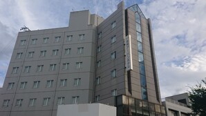 Un hôtel à plusieurs étages, doté d’un design moderne, avec une combinaison de fenêtres rectangulaires et carrées, et une façade en verre remarquable sur un de ses côtés.